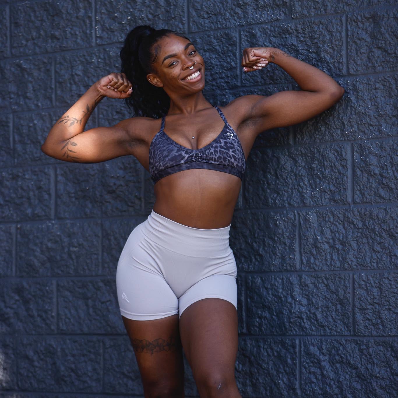 Jalynn smiling and flexing both arms in front of a dark brick wall